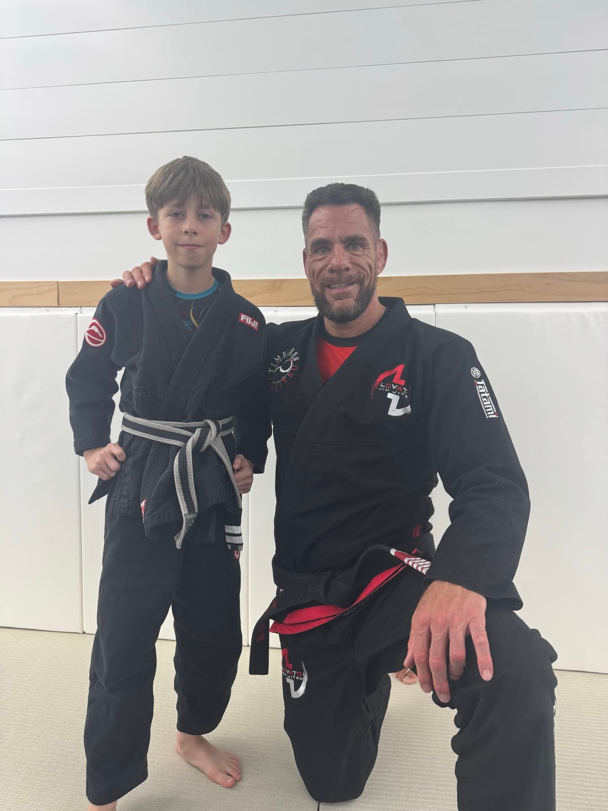 Ethan, in his black gi and grey-and-white belt, standing with Professor Rafael Lovato Jr. on the mats